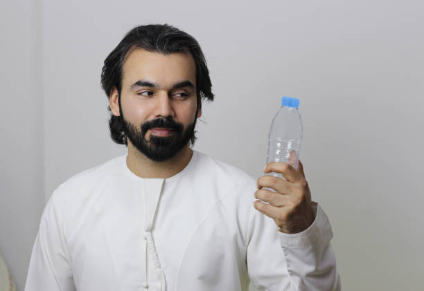 An Arab man holding a replaceable water bottle and looking into it